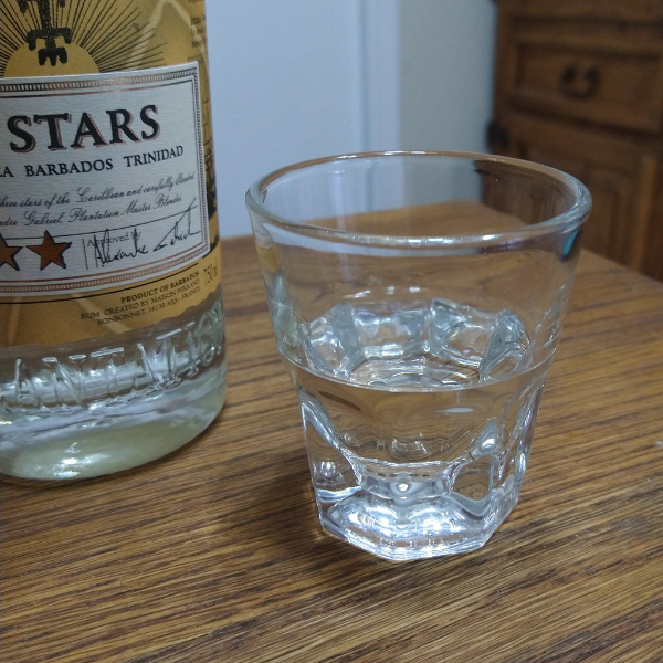 Small cup of clear rum, next to the label portion of a bottle of Plantation 3 Star White Rum