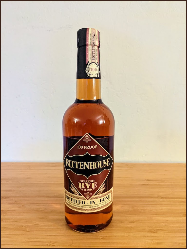 Rittenhouse Rye Bottled-In-Bond bottle with brown liquid on a light brown table with a white background