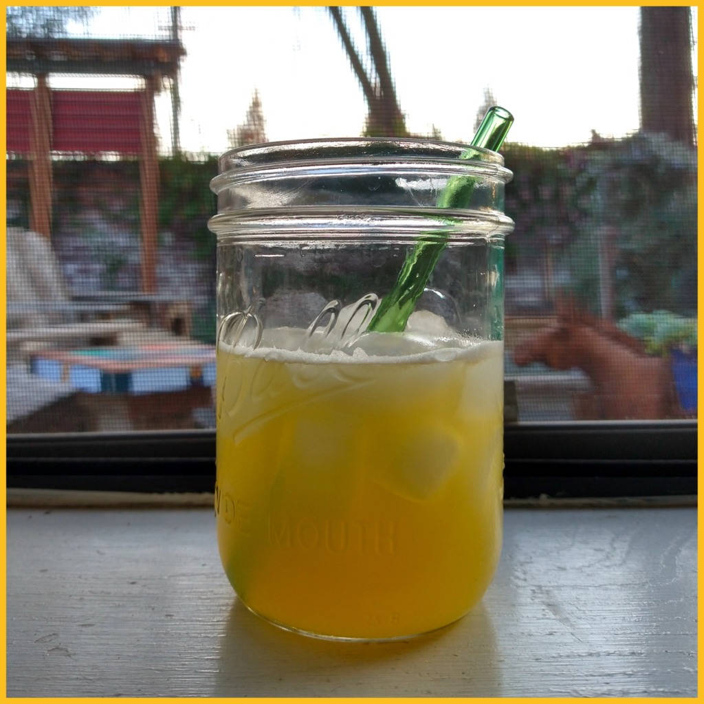 Matador cocktail in a clear Ball jar with a green glass straw, sitting on a white windowsill with a large yard in the background