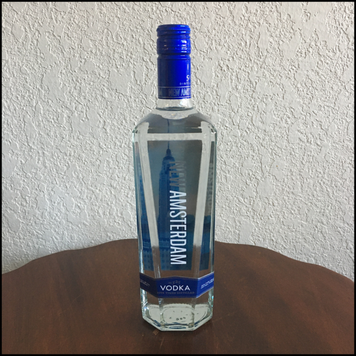 Bottle of New Amsterdam Original Vodka sitting on a dark brown table in front of an off-white wall