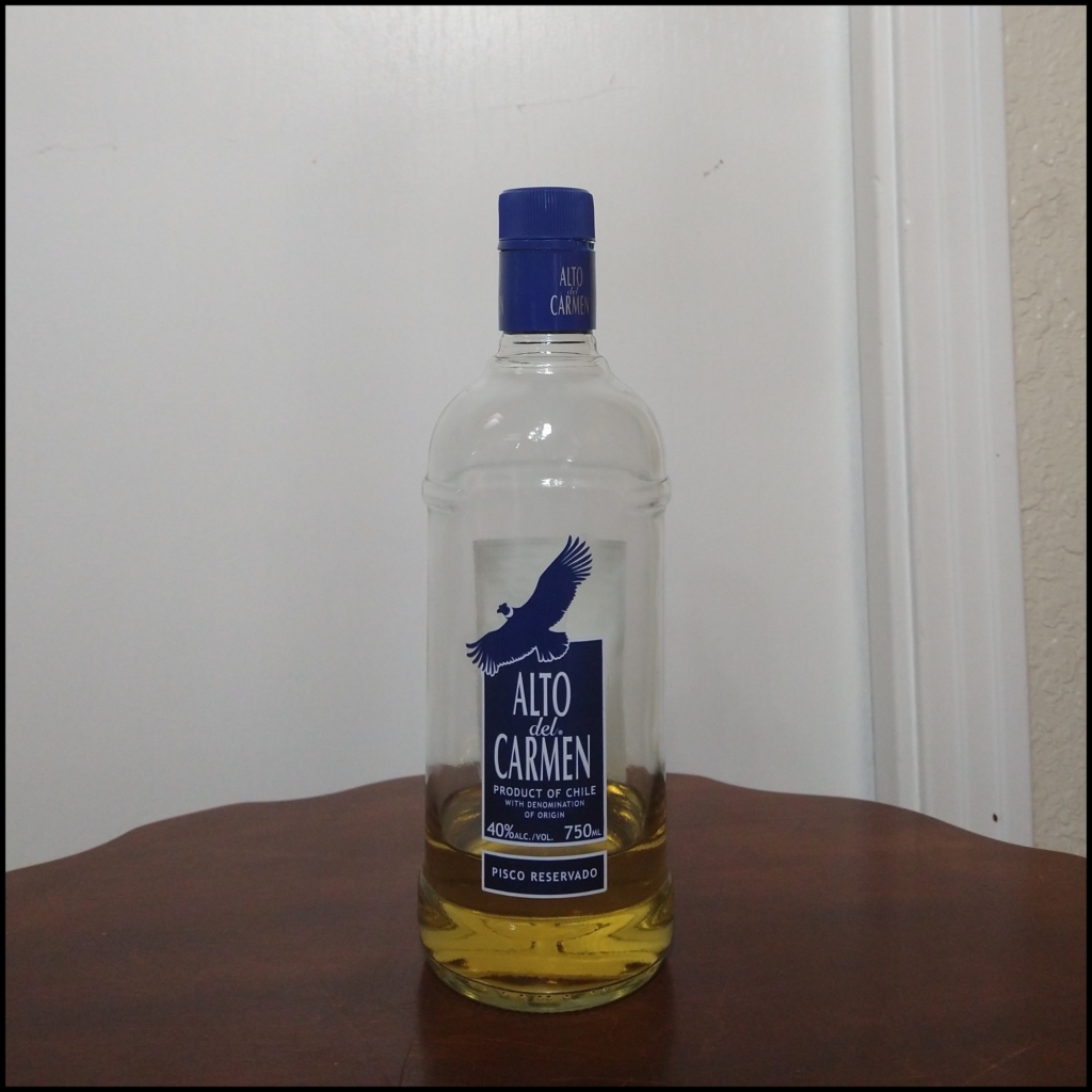 Bottle of Alto del Carmen Pisco Reservado sitting on top of a dark brown table, in front of a white door
