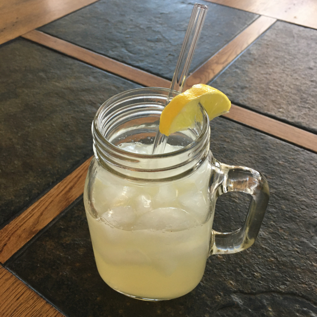 Moscow Mule cocktail in a glass mug with a clear glass straw, on top of a dark grey stone and wooden table