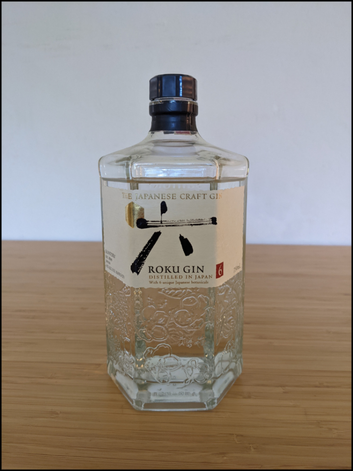 Clear Roku Gin bottle with clear liquid on a light brown table with a white background