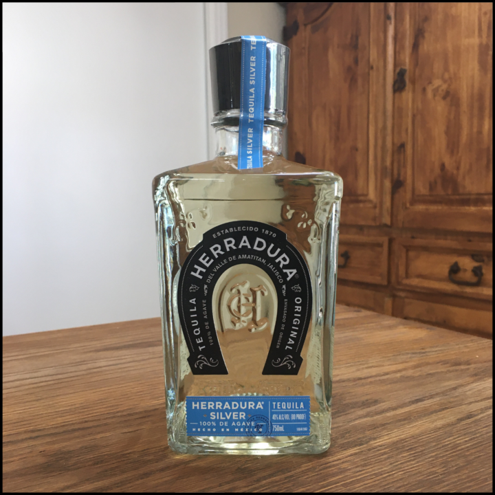 Bottle of Herradura Silver Tequila on a wooden table, in front of a mixed white and wooden background