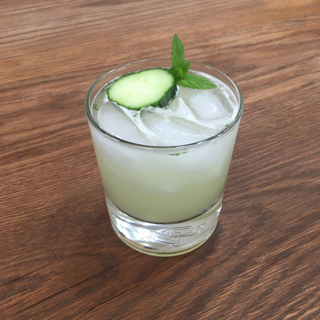 Tequila Eastside cocktail in a short cocktail glass with cucumber and mint sprig garnish, on a wooden table