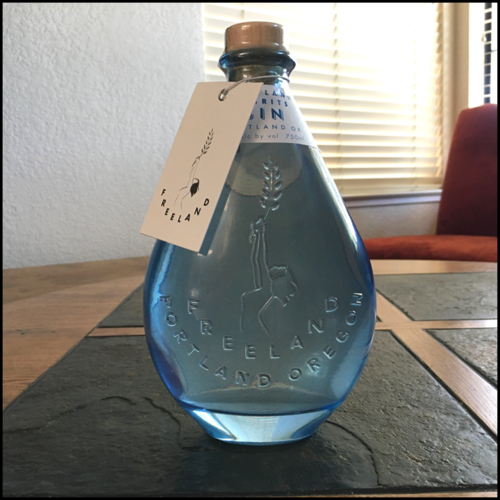 Blue, teardrop-shaped bottle of Freeland Spirits Gin, sitting on a mixed wood and stone table
