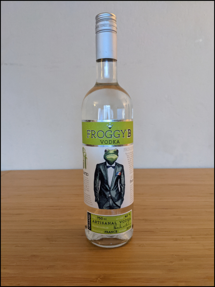 tall clear bottle with a clear liquid with alight green color and a frog in a suit and tie on the label