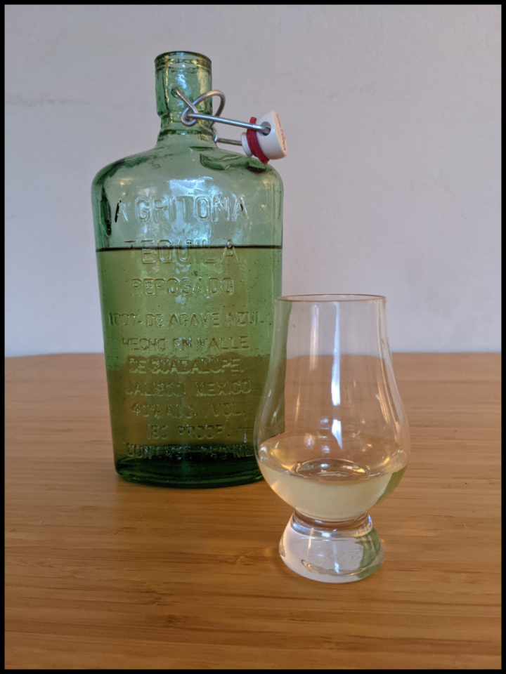 light yellow liquid in a glencarin glass with a green bottle in the background