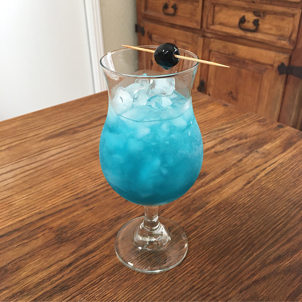 Bright aqua blue cocktail with crushed ice in a curvy cocktail glass with cherry garnish