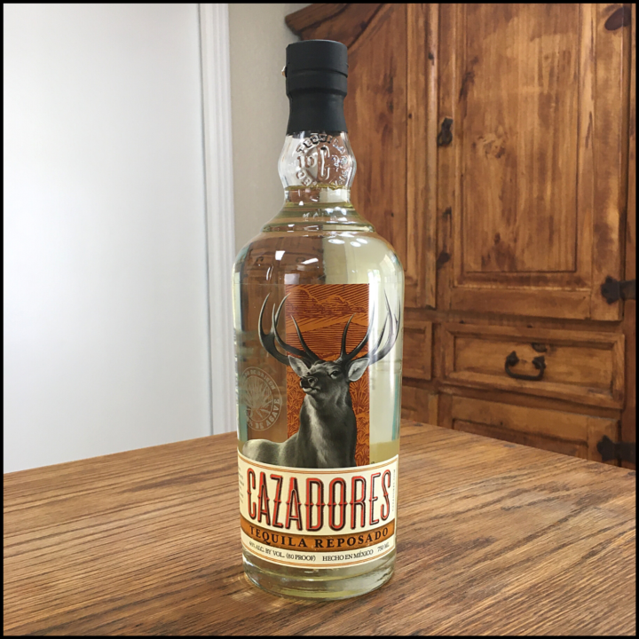 Bottle of Cazadores Tequila Reposado sitting on a wooden table, in front of a mixed white and wooden background