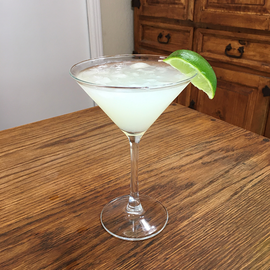 Green-white cocktail in a martini glass with lime wedge garnish, sitting on a wooden table
