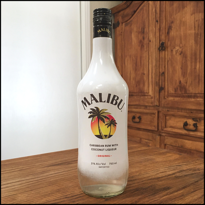 Bottle of Malibu Coconut Rum sitting on a wooden table, in front of a mixed white and wooden background