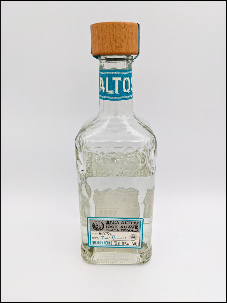 tall clear bottle with embossed lettering and a blue bordered label with at large wood cap