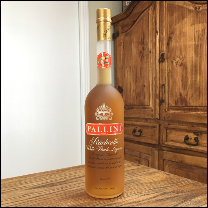 Bottle of orange-hued Peachcello liqueur sitting on a wooden table, in front of a mixed white and wood background
