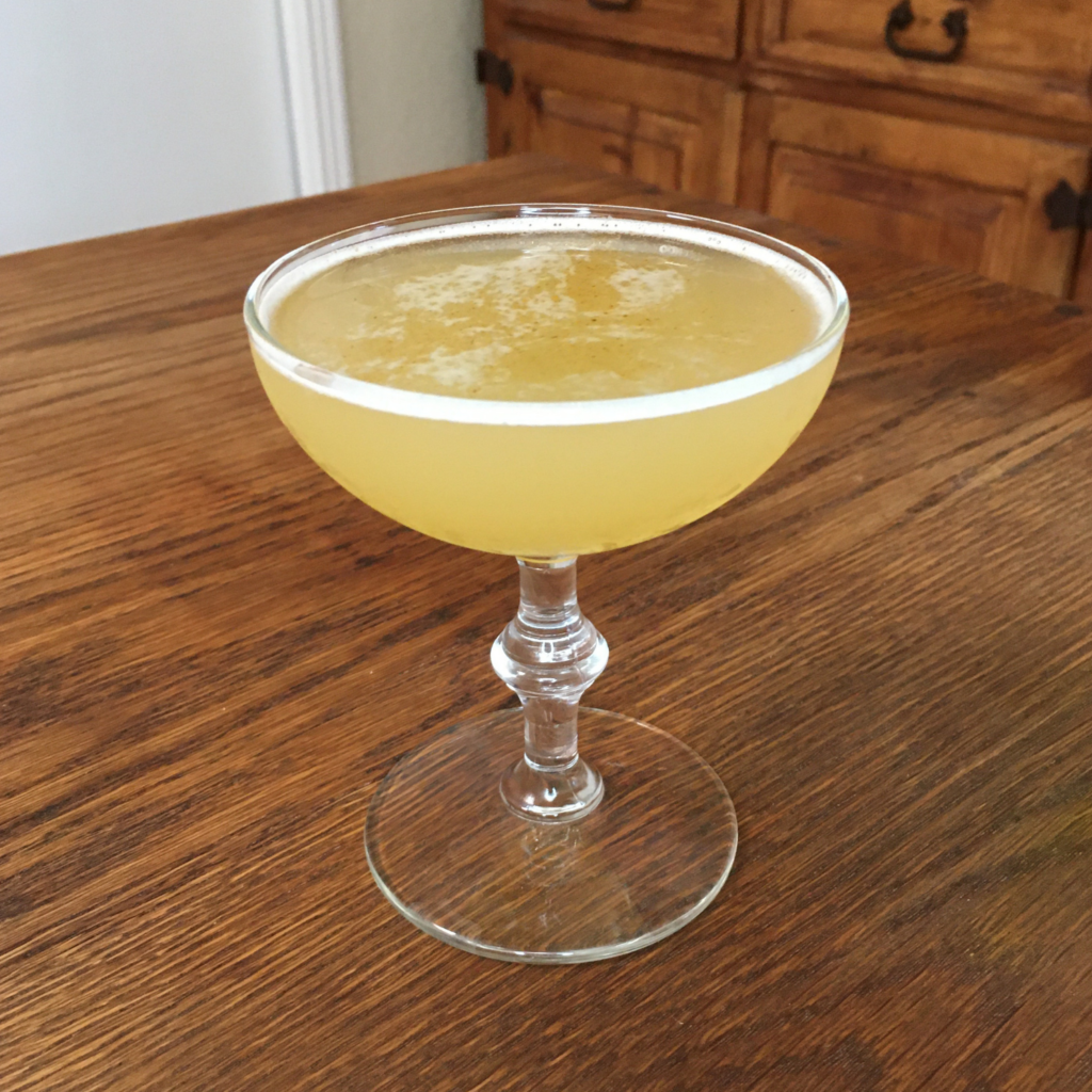 Golden yellow colored cocktail in a coupe glass with cayenne pepper garnish