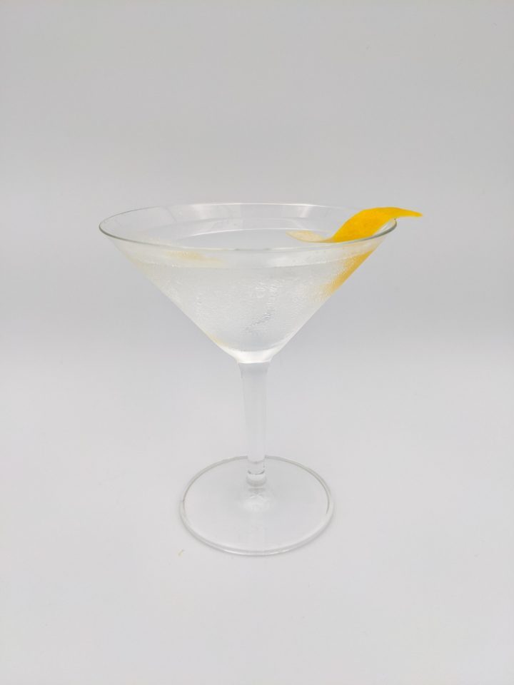 Clear liquid in a martini glass with a lemon twist hanging off the edge of the rim