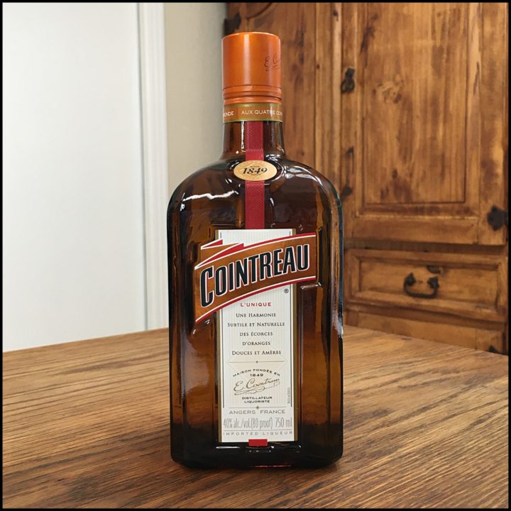 Bottle of Cointreau orange liqueur sitting on a wooden table, in front of a mixed white and wooden background