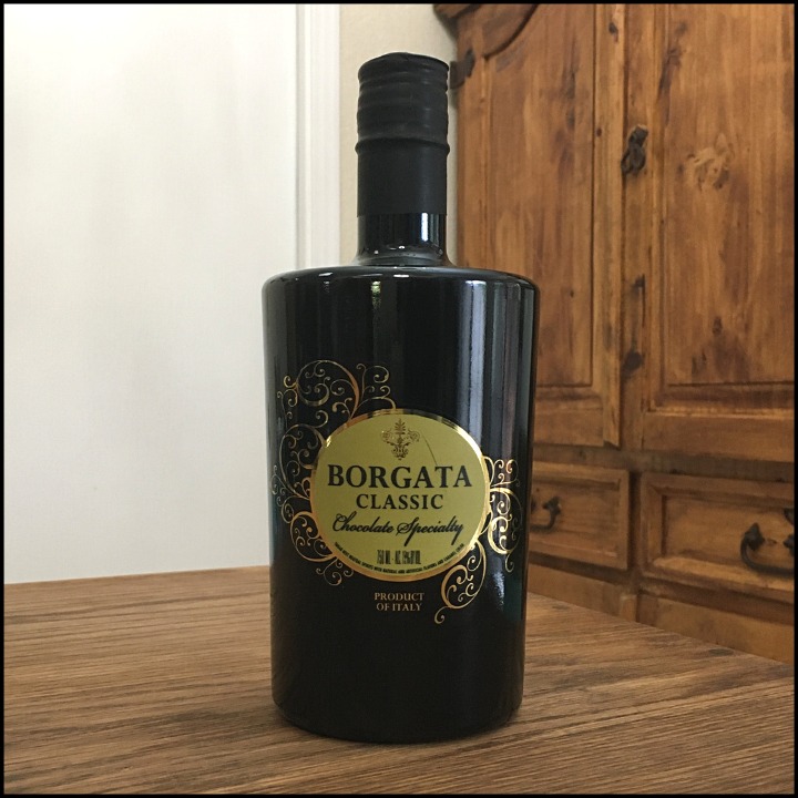 Bottle of Borgata Chocolate Liqueur sitting on a wooden table, in front of a mixed white and wooden background