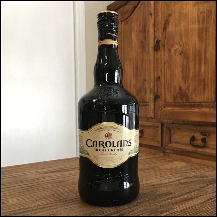 Bottle of Carolans Irish Cream sitting on a wooden table, in front of a mixed white and wooden background