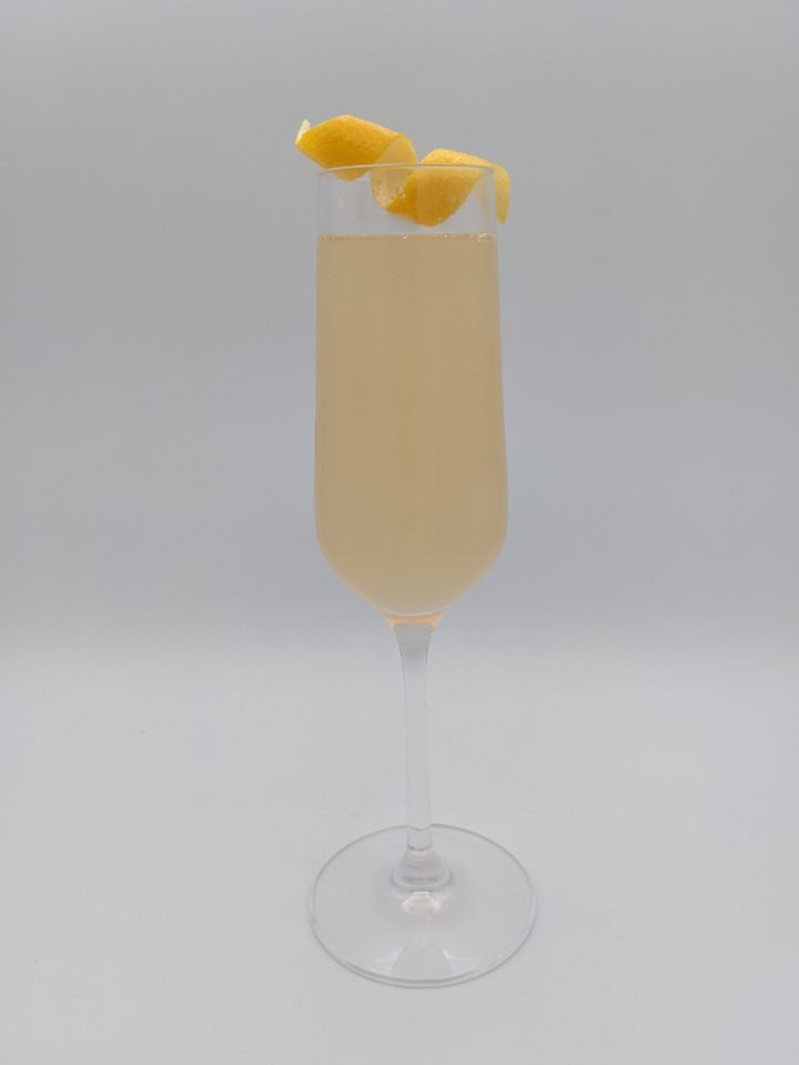 pale gold liquid in a long stemmed champagne flute with a curled lemon peel garnish