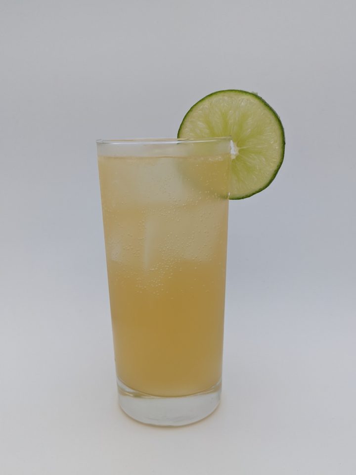 golden yellow liquid in a tall collins glass with a lime wheel as garnish