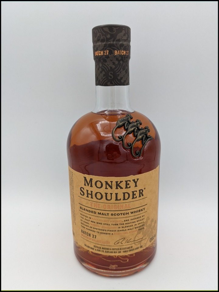 golden brown liquid in a round bottle with a tall neck with three monkeys on the bottle