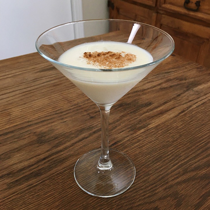 Martini glass filled with a creamy white cocktail with ground cinnamon garnish, sitting on a wooden table