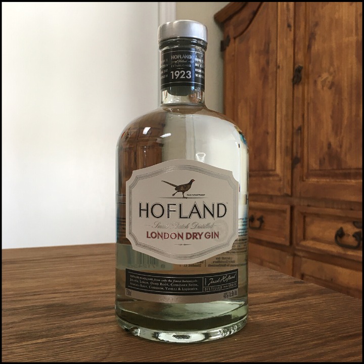 Bottle of Hofland Gin sitting on a wooden table, in front of a mixed white and wooden background