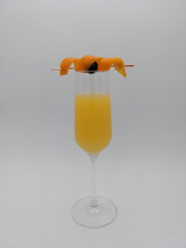 orange liquid in a champange flute with a orange peel and cherry garnish