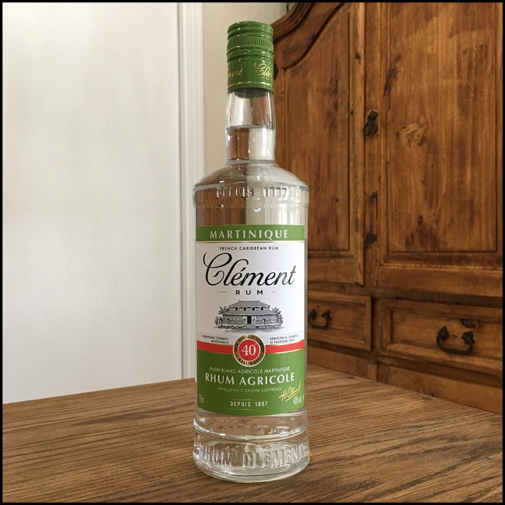 Bottle of Clément Rhum Agricole Blanc sitting on a wooden table, in front of a mixed white and wooden background