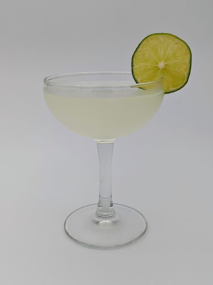 Light green liquid in a coupe glass with a wheel of lime as garnish
