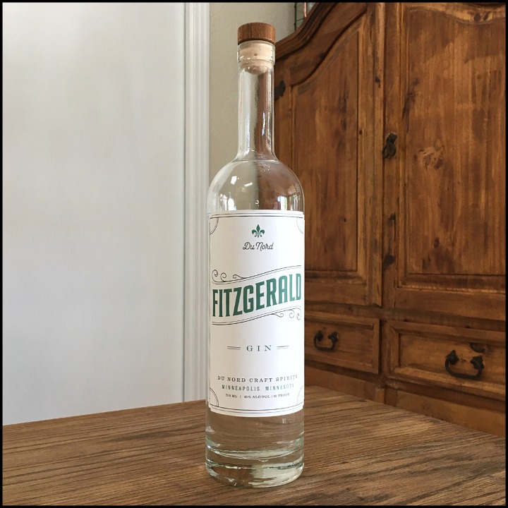 Bottle of Du Nord Fitzgerald Gin sitting on a wooden table, in front of a mixed white and wooden background