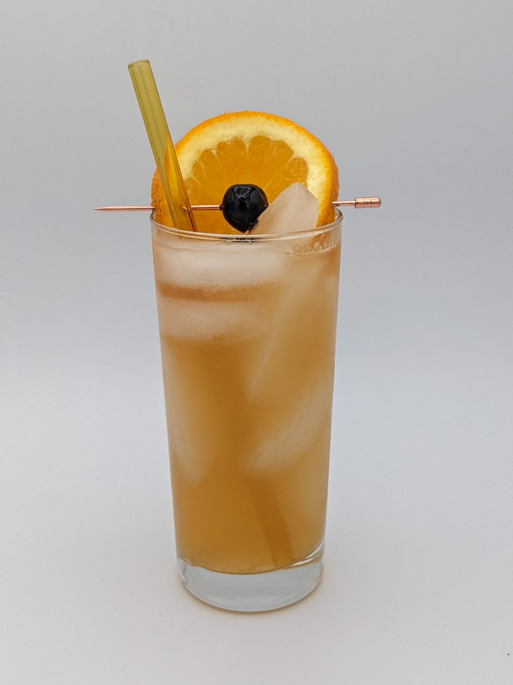 golden liquid in a collins glass filled with ice and garnished with a cherry and orange slice
