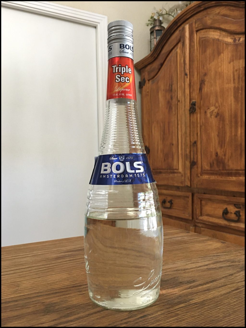 Bottle of Bols Triple Sec sitting on a wooden table, in front of a mixed white and wooden background