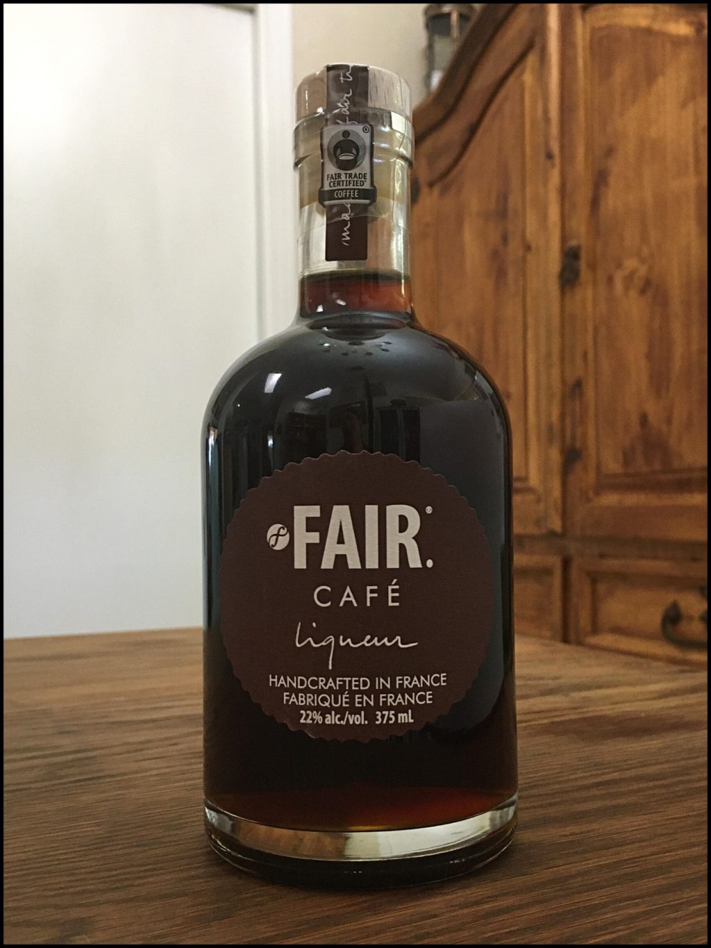 Bottle of Fair Cafe Liqueur sitting on a wooden table, in front of a mixed white and wooden background