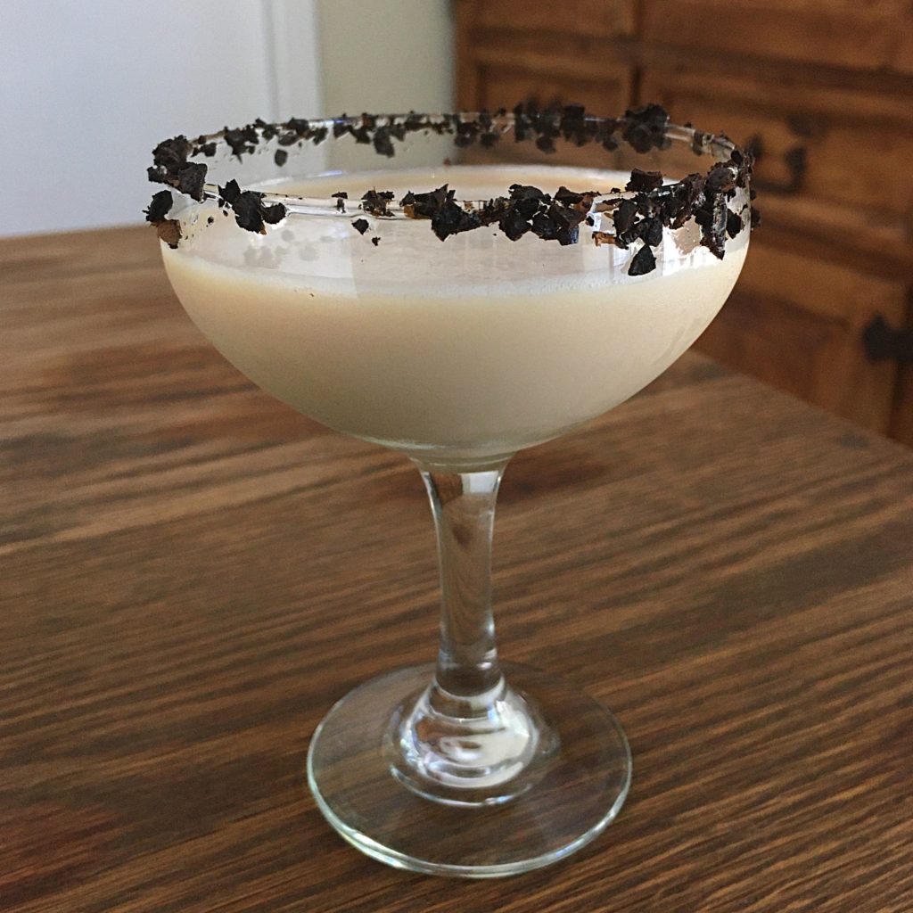 Light brown creamy cocktail in a coupe glass rimmed with crushed coffee beans