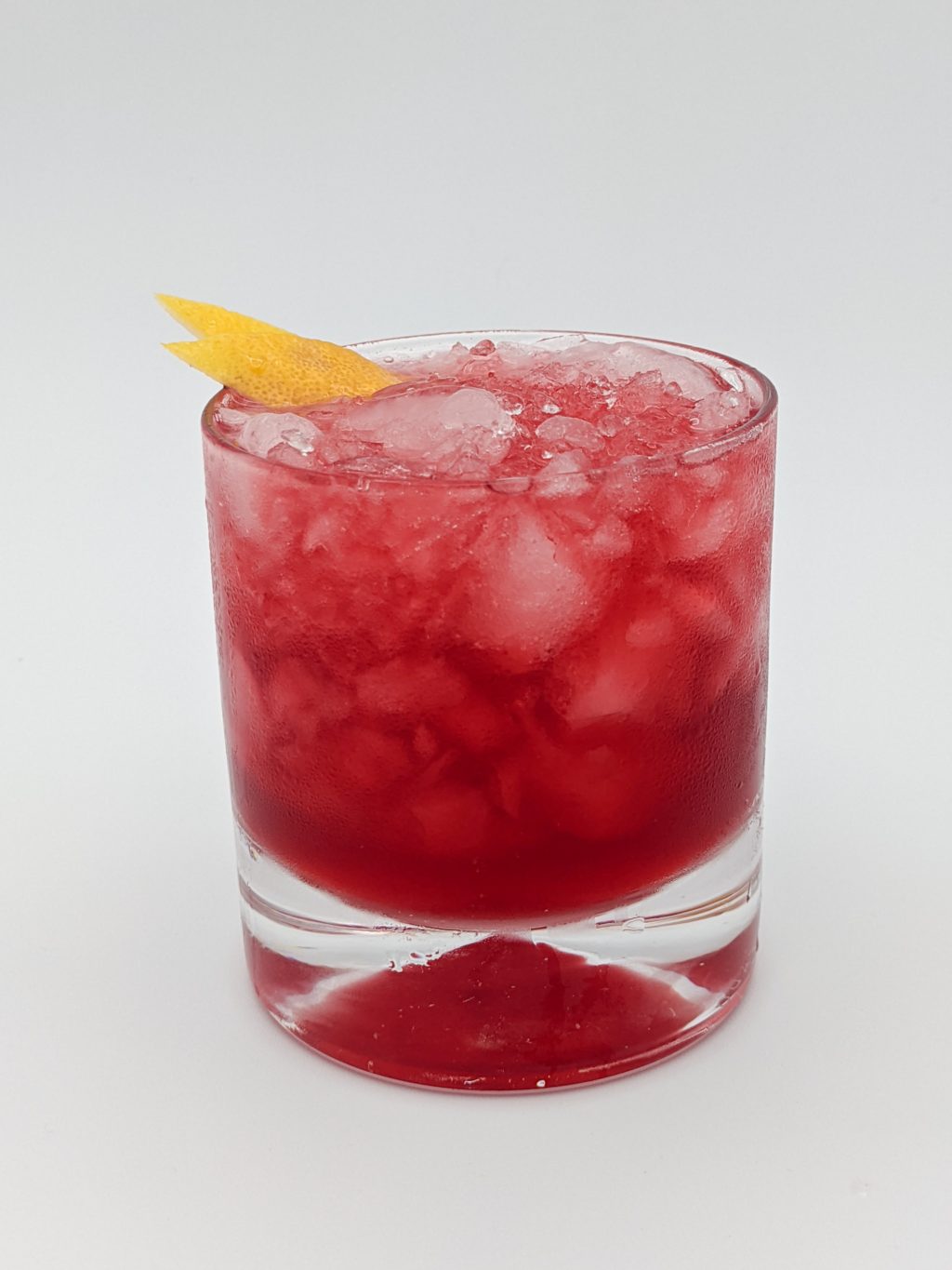 Dark red liquid in a rocks glass filled with crush ice with a lemon peel garnish