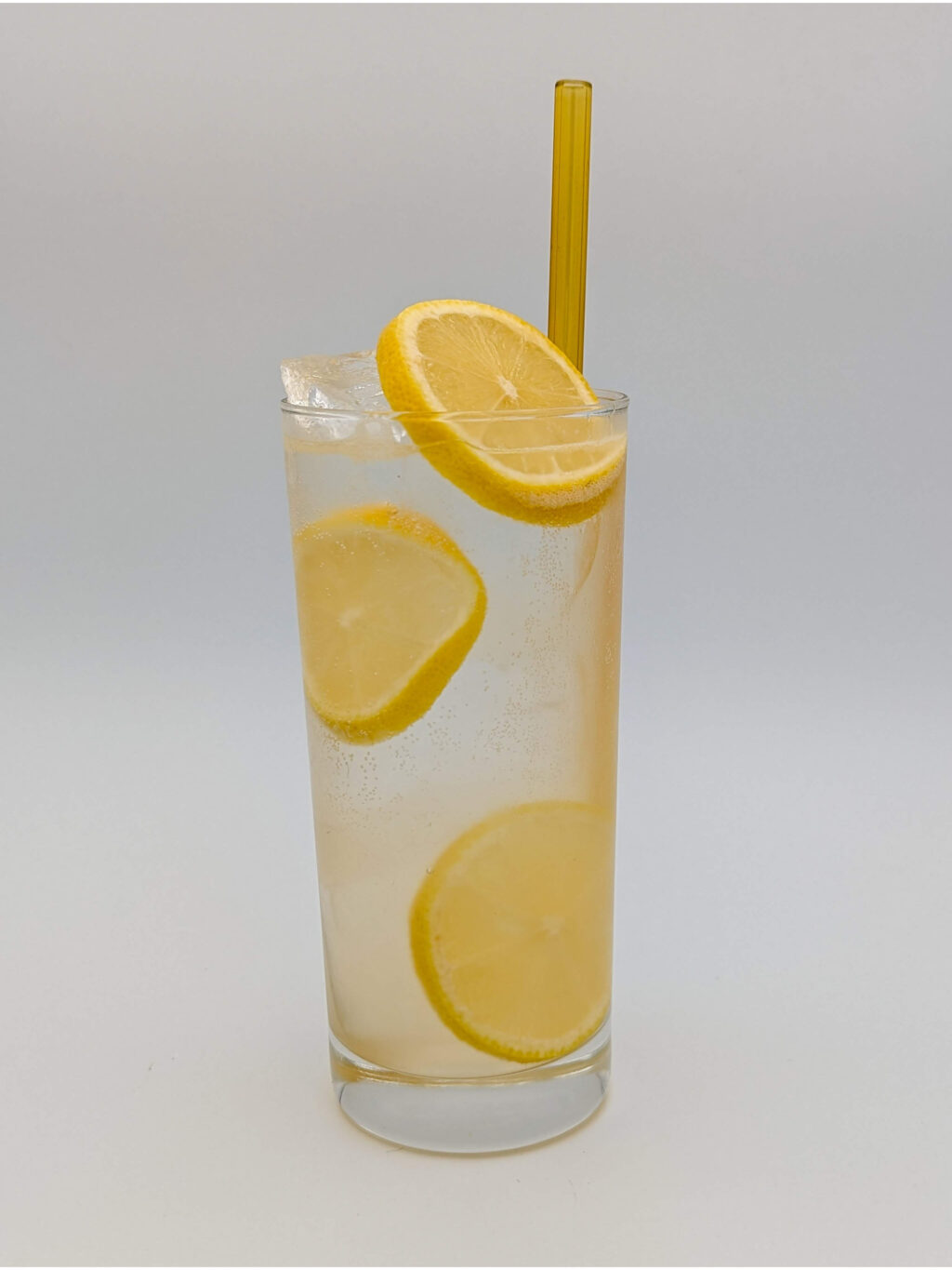 Light yellow liquid in a tall glass with large slices of lemon