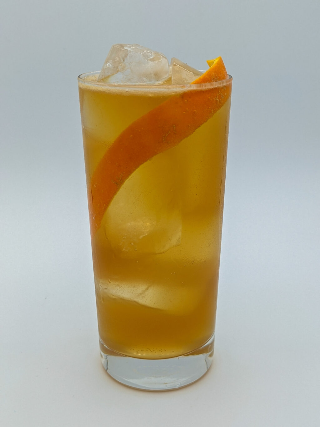 golden liquid in a highball glass filled with ice with a long orange peel garnish