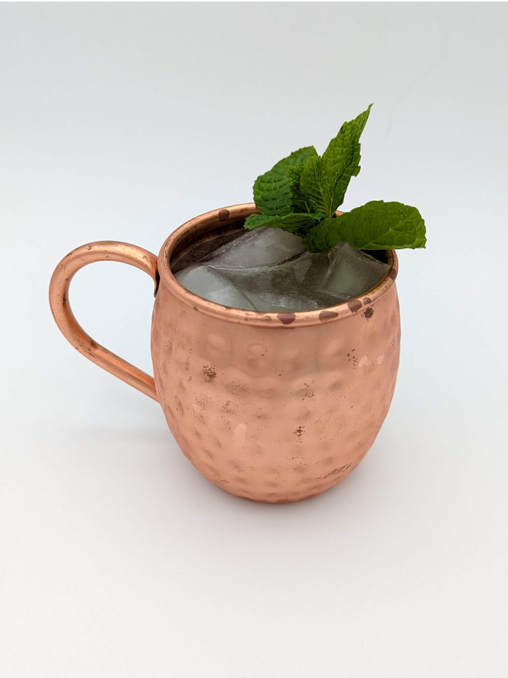 Fizzy liquid and ice in a copper mug with a sprig of mint as garnish