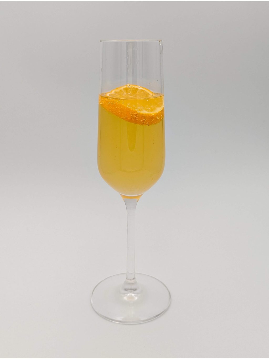 orange liquid in a champagne flute with a slice of lemon for garnish