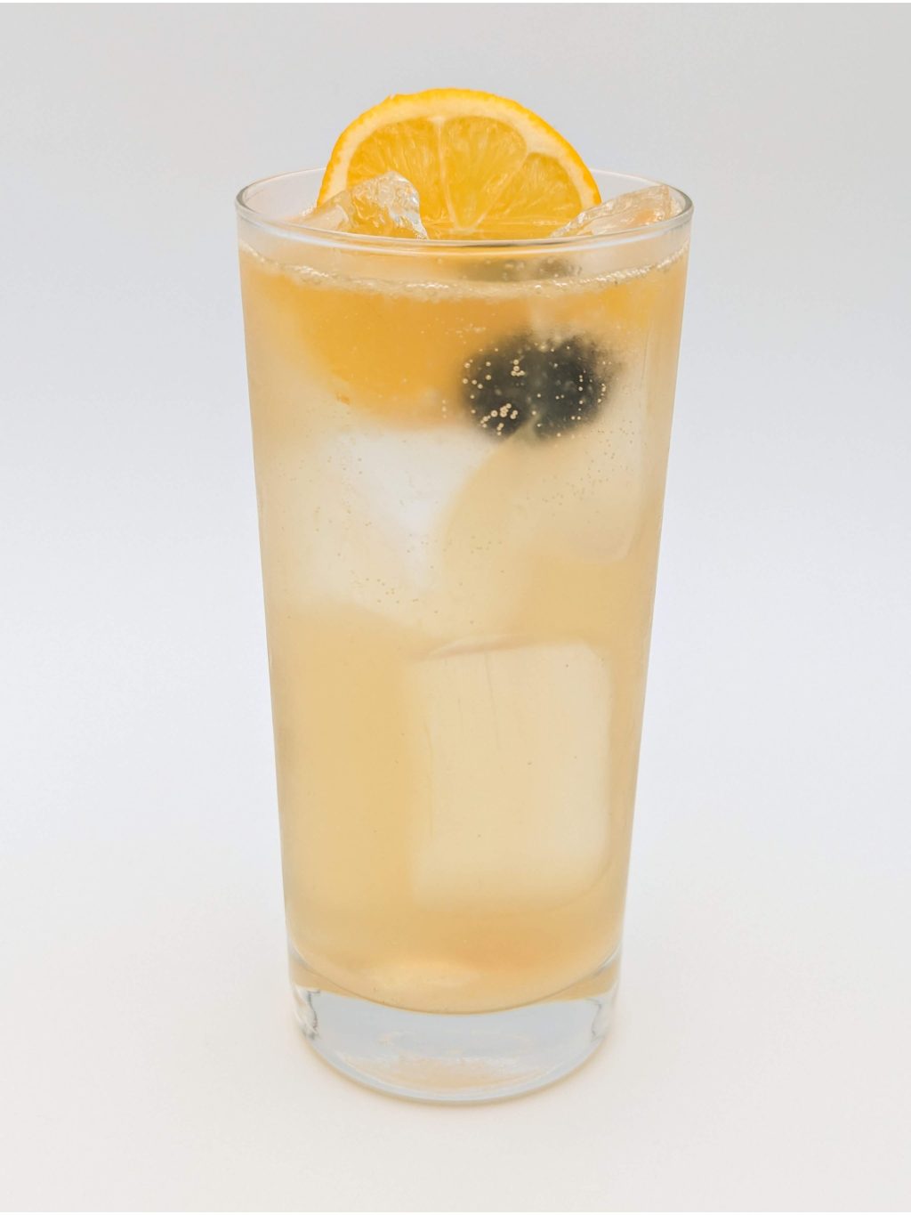 yellow liquid in a tall glass with ice and a lemon slice and cherry garnish