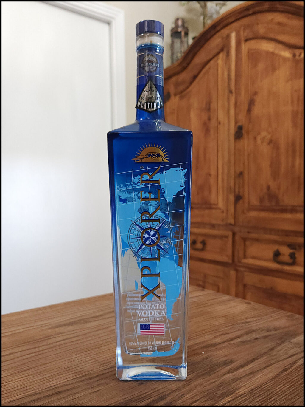 Bottle of Xplorer Potato Vodka sitting on a wooden table, in front of a mixed white and wooden background