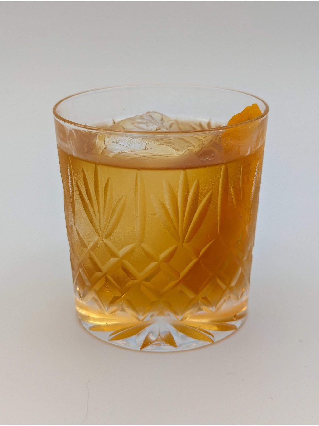 light golden brown liquid in a crystal glass with a large rock of ice and lemon peel garnish