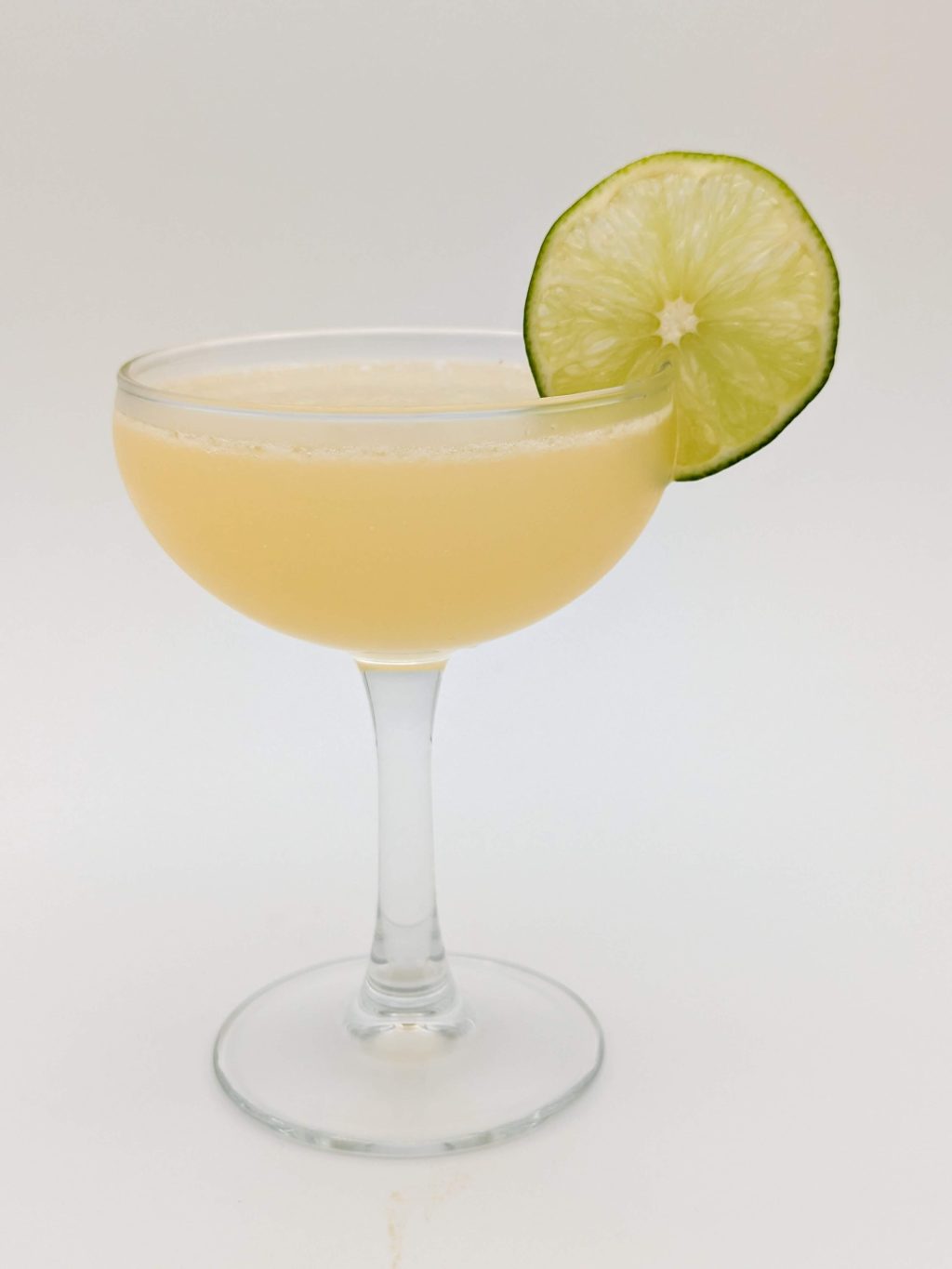 yellow green liquid in a coupe glass with a lime wheel garnish