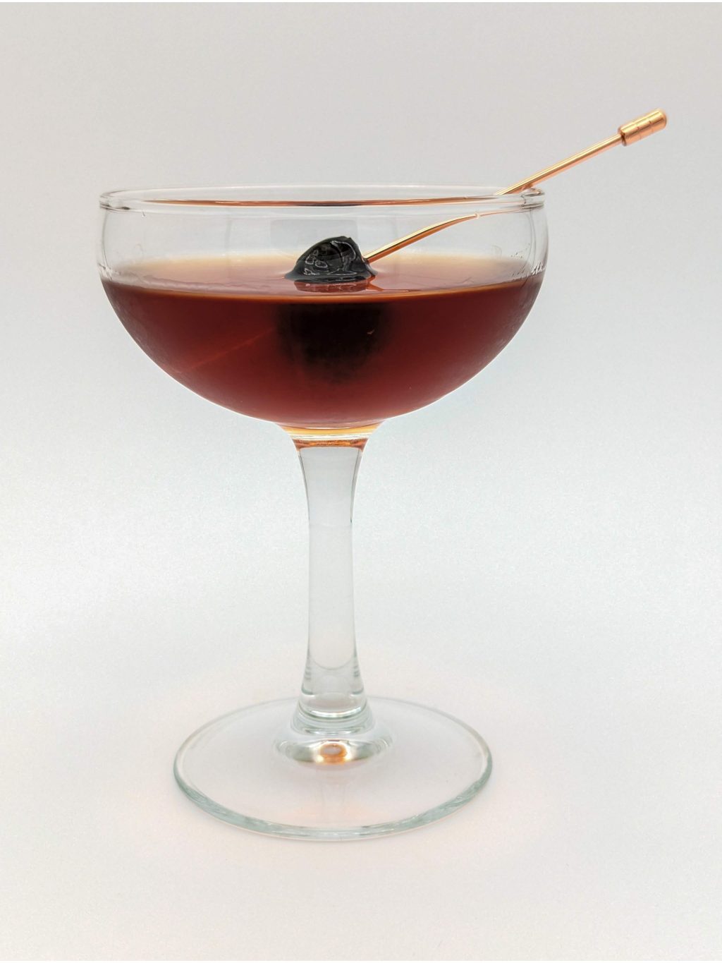 dark amber liquid in a coupe glass with a cherry for garnish