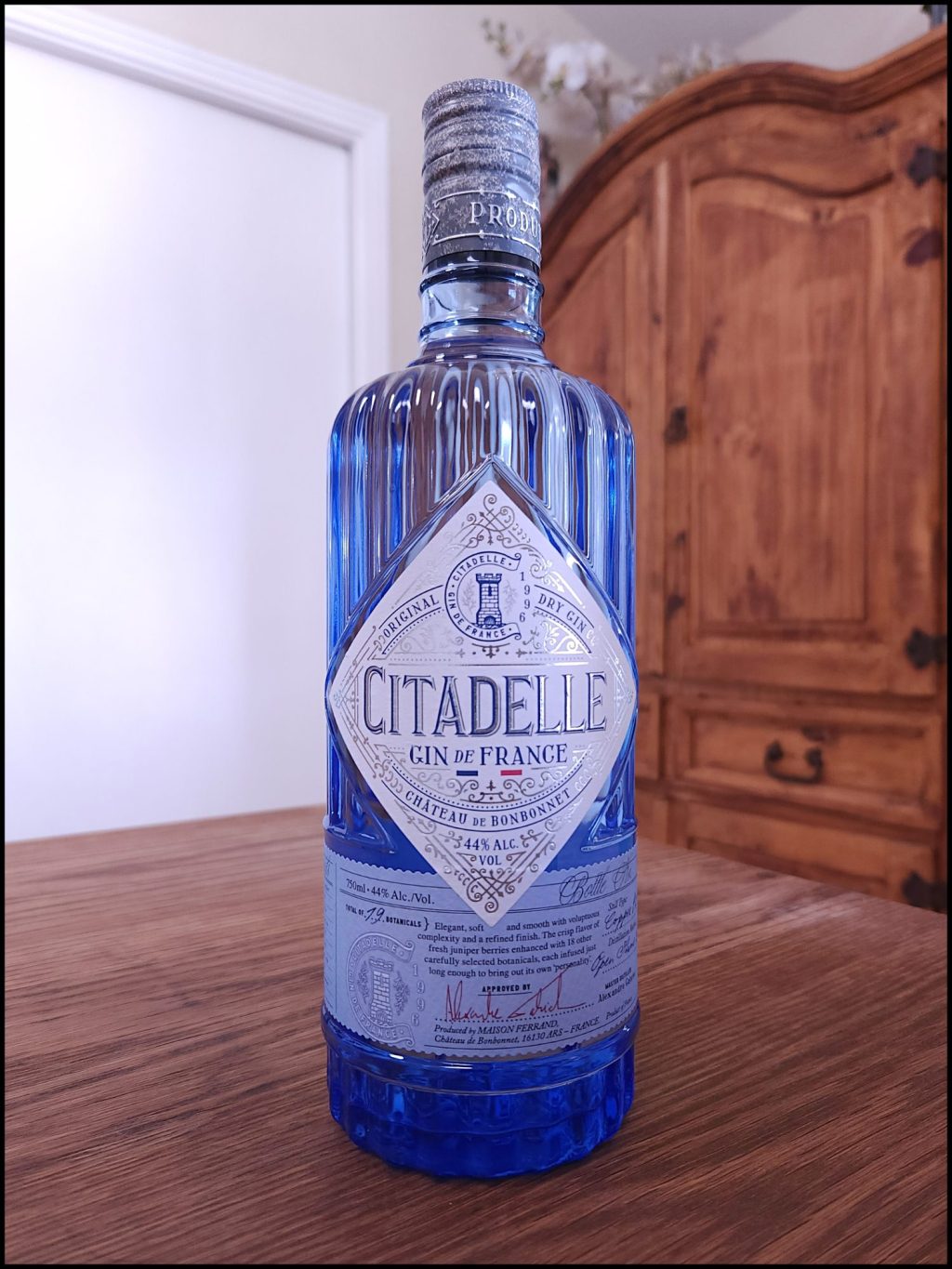 Bottle of Citadelle Original Gin on a wooden table, in front of a mixed white and wooden background