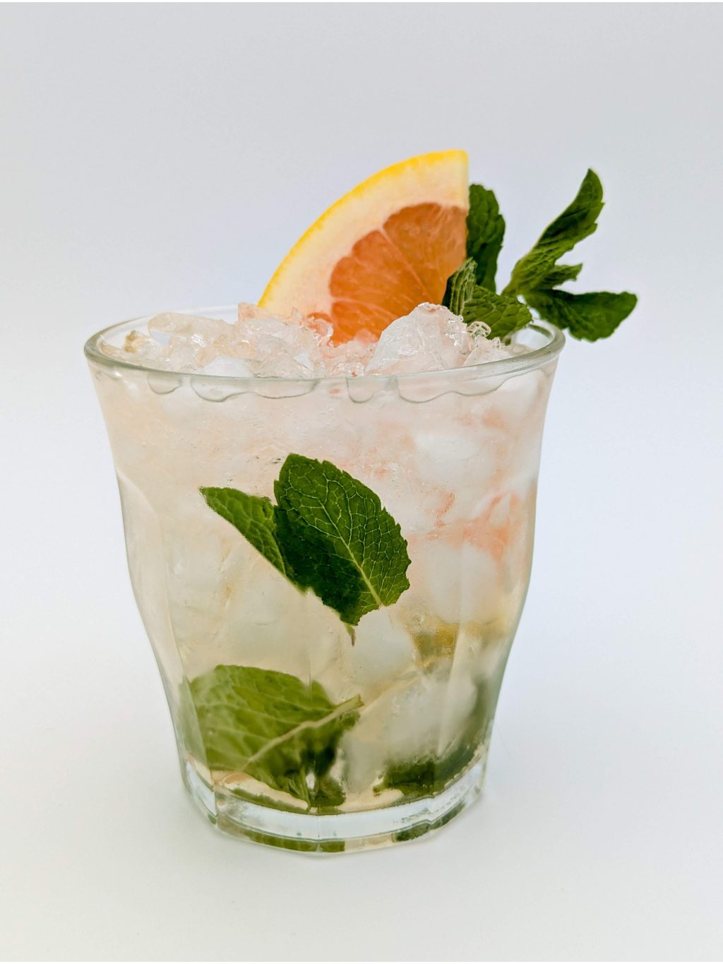 slightly gold liquid and mint leaves in an old fashioned glass filled with crushed ice with a grapefruit slice and mint as garnish