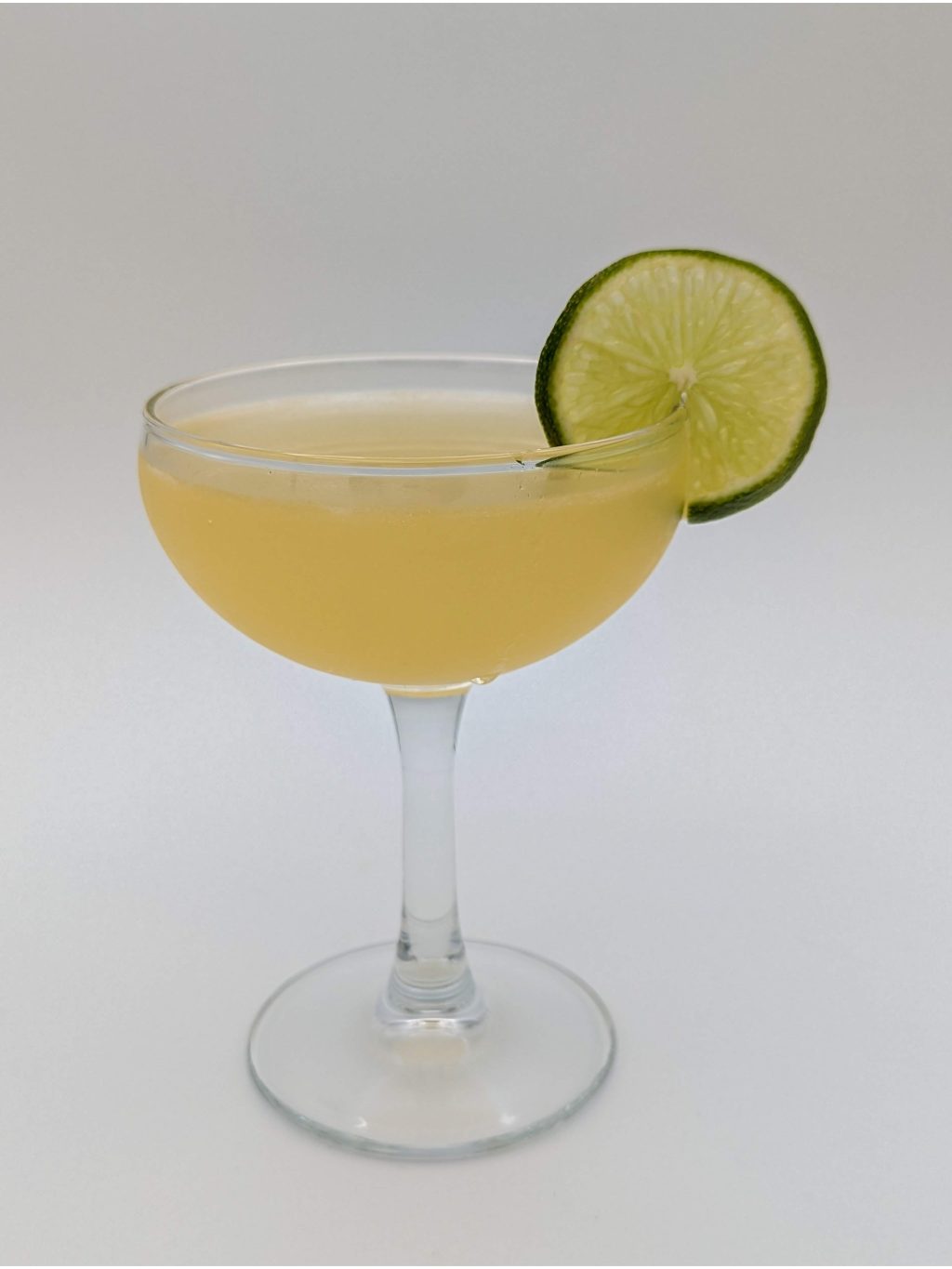 gold liquid in a coupe with a lime wheel as garnish