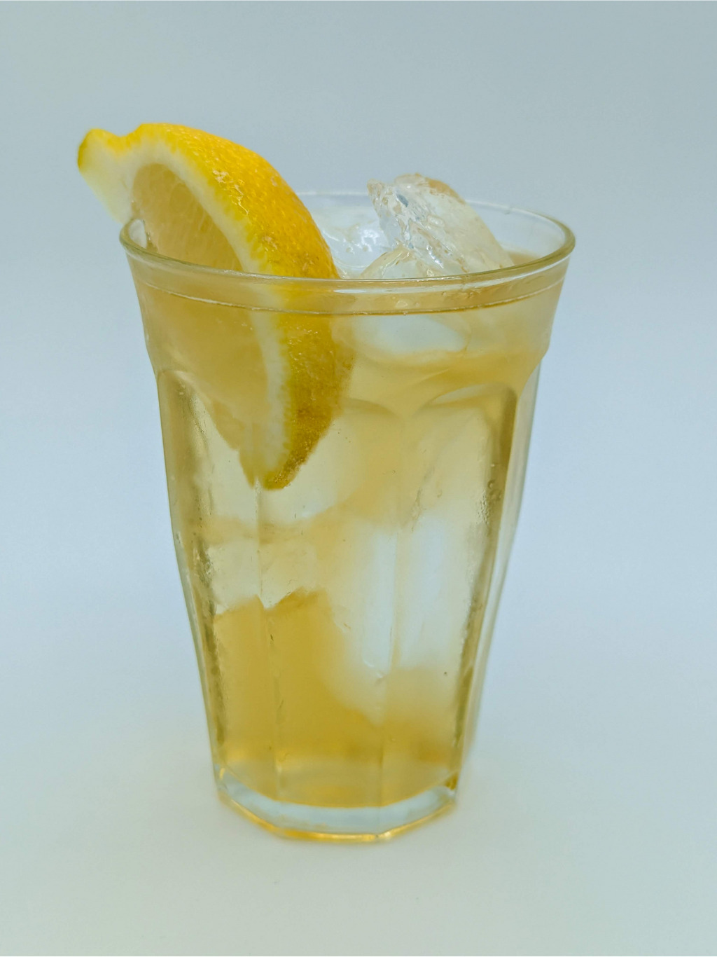 yellow liquid in a clear glass filled with ice and garnished with a lemon wedge